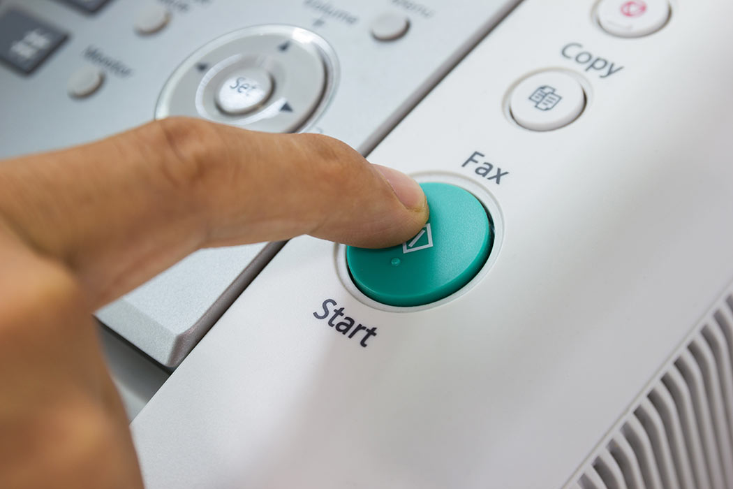 Closeup of someone's finger pushing "start" button on fax machine