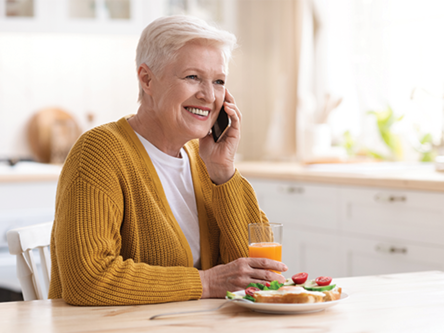 Senior woman smiling with a phone held to her ear and holding a glass of juice
