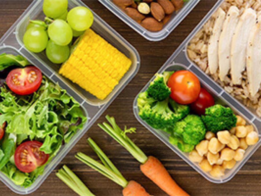 Bird's eye view of packed meals and salads in food containers on a dark wooden table